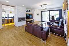 Obývací pokoj je oddělen od kuchyně skleněnými dveřmi, které se zasouvají do stěny. Třívrstvá dřevěná podlaha zahřívá interiér svým vzhledem i fakticky – v domě je instalováno podlahové topení