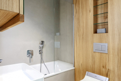 V koupelnách je dubové dřevo kombinováno s bílou sanitou, cementovými stěrkami a velkoformátovou dlažbou imitující beton