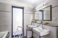 Také koupelna se světlými šedavými obklady a hnědou dlažbou ctí barevnou linii interiéru domu